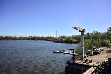 Güneşli bir günde yanında bir orman bulunan sanayi kompleksi olan göl kıyısında bir liman.