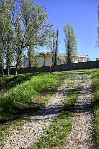 Path on an embankment next to a boundary wall of an industrial complex in a forest