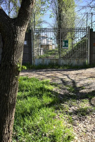 Gate in a concrete boundary wall of a factory by the edge of a path in a park
