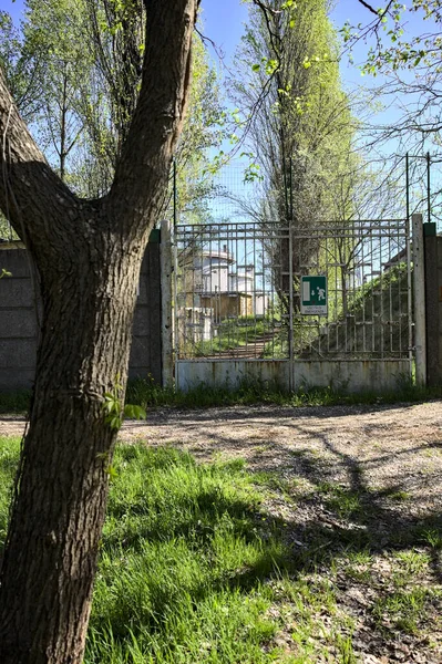 Gate in a concrete boundary wall of a factory by the edge of a path in a park