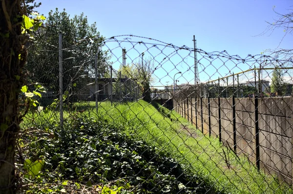 Concrete boundary wall and a fence with a industrial complex in the background behind them