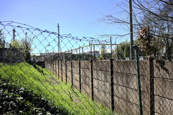 Concrete boundary wall and a fence with a industrial complex in the background behind them