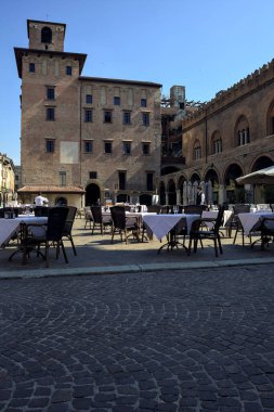 Güneşli bir günde İtalyan kasabasında gezen insanlarla dolu bir meydan.