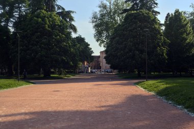 İtalya 'nın bir şehrinde gün batımında bir parkta ağaçlar ve çimlerle çevrili çakıl yolu.
