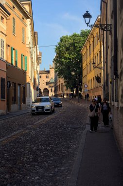 Gün batımında bir italyan kasabasında yüksek binalarla ve arabalarla çevrili bir cadde.