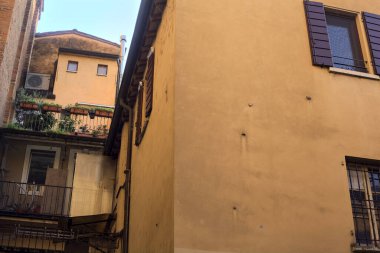 Gün batımında İtalyan kasabasında gölgeli bir sokağa yerleştirilmiş saksı bitkileriyle dolu küçük bir balkon.