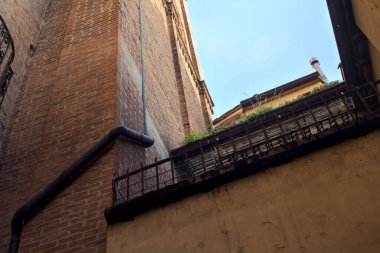 Gün batımında İtalyan kasabasında gölgeli bir sokağa yerleştirilmiş saksı bitkileriyle dolu küçük bir balkon.