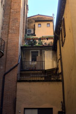 Gün batımında İtalyan kasabasında gölgeli bir sokağa yerleştirilmiş saksı bitkileriyle dolu küçük bir balkon.