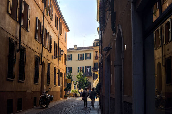 Narrow and cobbled street in the shade with people strolling in an italian town at sunset