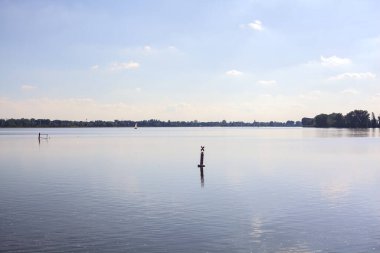 Gün batımında göl, suyun içinde gökyüzü ve uzaklarda bir yelkenli.