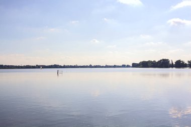 Gün batımında göl, suyun içinde gökyüzü ve uzaklarda bir yelkenli.