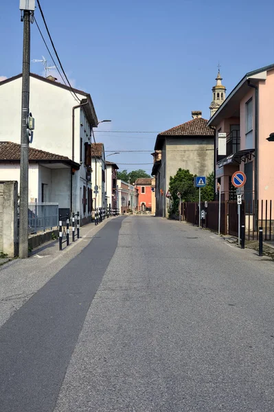 Road bordered by houses with a church at the end of it on a sunny day in a village in the italian countryside