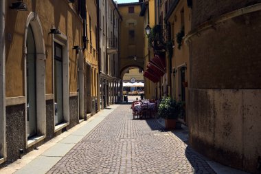 Bir İtalyan şehrinde güneşli bir günde, bir restoranın masaları ve sandalyeleriyle gölgede.