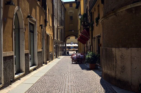 イタリアの町で晴れた日にレストランのテーブルと椅子がある日陰の一部に路地 — ストック写真