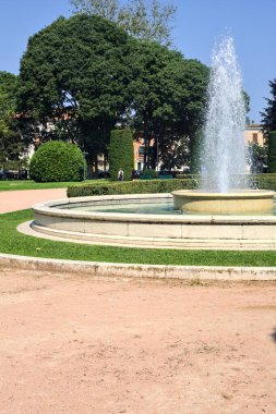 Güneşli bir günde, bir İtalyan kasabasındaki bir parkın meydanındaki çeşme.
