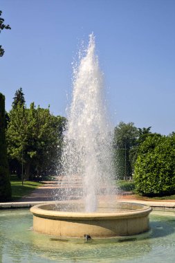 Güneşli bir günde, bir İtalyan kasabasındaki bir parkın meydanındaki çeşme.