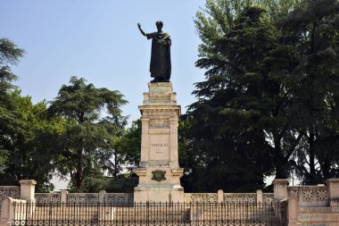 Güneşli bir günde parkta Publio Virgilio Marone anısına dikilmiş bir anıt.