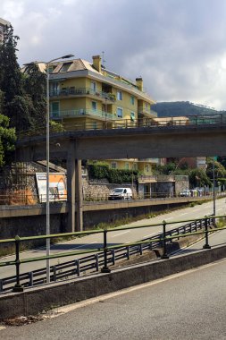 Gökdelenli bir otoyolda yükseltilmiş yollar ve bulutlu bir günde bir İtalyan şehrinde geçen arabalar.