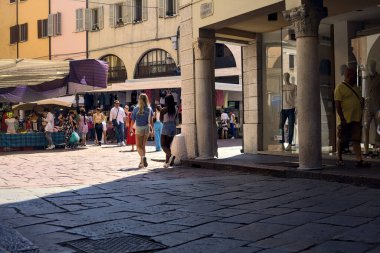 Güneşli bir günde, güneşli bir günde, gölgedeki bir verandadan insanların geçtiği bir meydan.