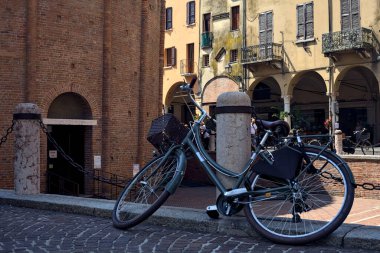 İtalyan kasabasında bir caddenin yanındaki meydanda bir direğe yaslanan bisiklet.