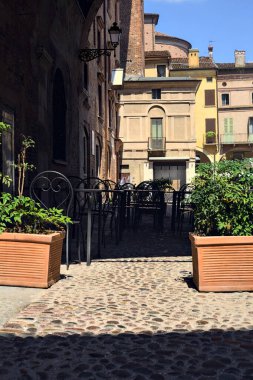 Güneşli bir günde İtalya 'da bir meydanda bir binanın kemerinin altında masa ve sandalyeler.