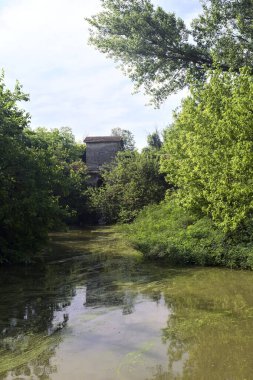 Ağaçlı bir gölet ve karşı kıyısında eski bir baraj. İtalya 'nın kırsal kesiminde bir yaz günü.