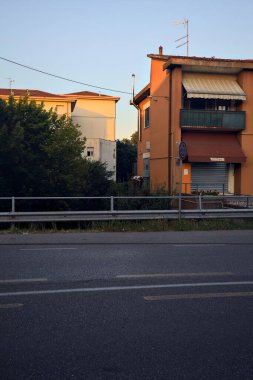 Gün batımında İtalya kırsalında iki binayla çevrili bir su deresinin üzerindeki yol.