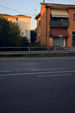 Gün batımında İtalya kırsalında iki binayla çevrili bir su deresinin üzerindeki yol.