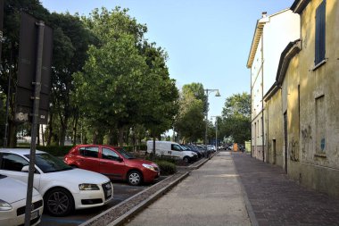 Gün batımında bir İtalyan kasabasında, bir binanın ve park edilmiş arabaların yanında.