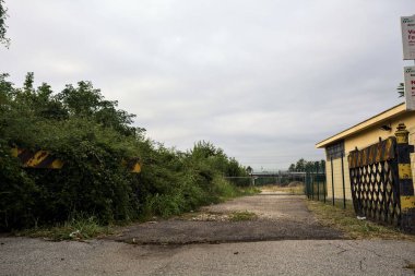 Yıpranmış çakıl yolu, İtalya 'nın kırsal kesimlerinde bulutlu bir günde tren raylarına çıkan çalılarla çevrili bir kapı tarafından kapatılmış.