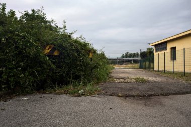 Yıpranmış çakıl yolu, İtalya 'nın kırsal kesimlerinde bulutlu bir günde tren raylarına çıkan çalılarla çevrili bir kapı tarafından kapatılmış.