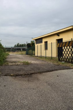 Yıpranmış çakıl yolu, İtalya 'nın kırsal kesimlerinde bulutlu bir günde tren raylarına çıkan çalılarla çevrili bir kapı tarafından kapatılmış.