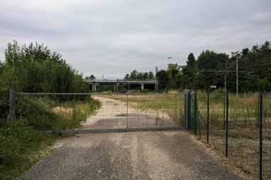 Yıpranmış çakıl yolu, İtalya 'nın kırsal kesimlerinde bulutlu bir günde tren raylarına çıkan çalılarla çevrili bir kapı tarafından kapatılmış.