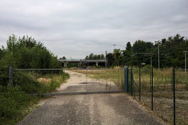 Yıpranmış çakıl yolu, İtalya 'nın kırsal kesimlerinde bulutlu bir günde tren raylarına çıkan çalılarla çevrili bir kapı tarafından kapatılmış.