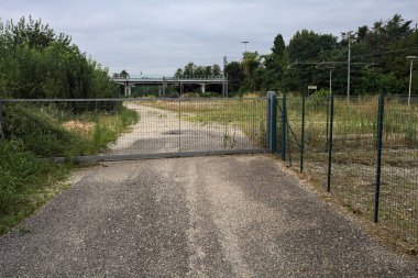 Yıpranmış çakıl yolu, İtalya 'nın kırsal kesimlerinde bulutlu bir günde tren raylarına çıkan çalılarla çevrili bir kapı tarafından kapatılmış.
