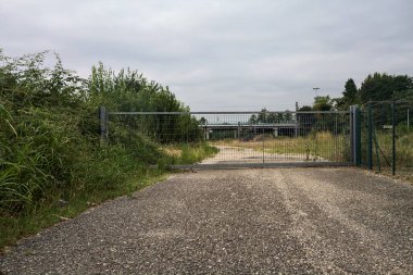 Yıpranmış çakıl yolu, İtalya 'nın kırsal kesimlerinde bulutlu bir günde tren raylarına çıkan çalılarla çevrili bir kapı tarafından kapatılmış.