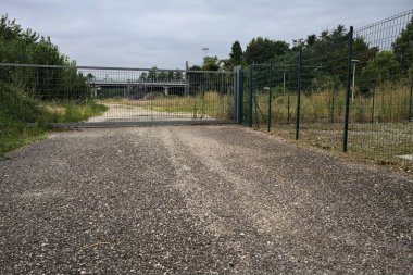 Yıpranmış çakıl yolu, İtalya 'nın kırsal kesimlerinde bulutlu bir günde tren raylarına çıkan çalılarla çevrili bir kapı tarafından kapatılmış.