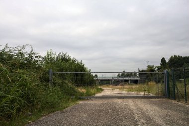 Yıpranmış çakıl yolu, İtalya 'nın kırsal kesimlerinde bulutlu bir günde tren raylarına çıkan çalılarla çevrili bir kapı tarafından kapatılmış.