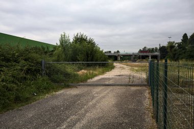 Yıpranmış çakıl yolu, İtalya 'nın kırsal kesimlerinde bulutlu bir günde tren raylarına çıkan çalılarla çevrili bir kapı tarafından kapatılmış.