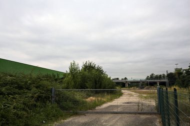 Yıpranmış çakıl yolu, İtalya 'nın kırsal kesimlerinde bulutlu bir günde tren raylarına çıkan çalılarla çevrili bir kapı tarafından kapatılmış.