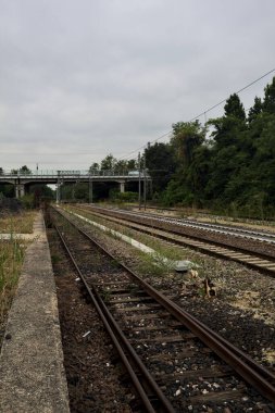 İtalya kırsalında bulutlu bir günde küçük bir viyadük altından geçen demiryolu rayların kenarından görülüyor.