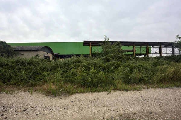 stock image Warehouse behind a fence and bushes on a cloudy day in the italian countryside seen from a dirt road