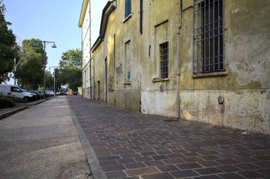 Gün batımında bir İtalyan kasabasında, bir binanın ve park edilmiş arabaların yanında.
