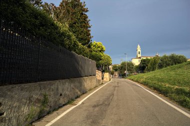 Dar bir tepede dar bir yol. Etrafı toprak ve çan kulesi ile çevrili.