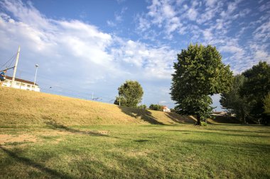 Gün batımında bir italyan kasabasının parkındaki bir toprak yığınının yanında kavak ağacı.