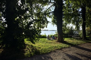 Gün batımında ağaçların altında, göl kıyısında oturan bir çift.