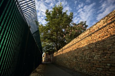 Günbatımında İtalya kırsalında, üzerinde ağaçlar olan bir çit ve tuğla duvar arasındaki yol.