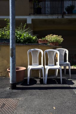 Gündüz vakti İtalya 'nın kırsal kesimindeki bir köyde bir evin sınır duvarının yanında plastik sandalyeler.