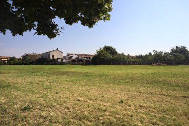 Bir ağaç tarafından çerçevelenmiş güneşli bir günde, zıt bir araziden görülen köy mahkemesi ve ahır.