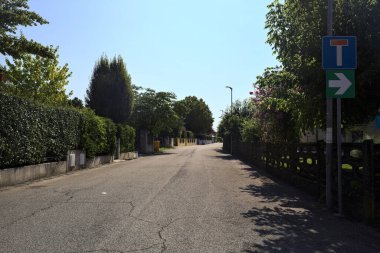 Güneşli bir günde İtalyan köyünün duvarlarında çitlerle ve bahçelerle çevrili bir sokak.